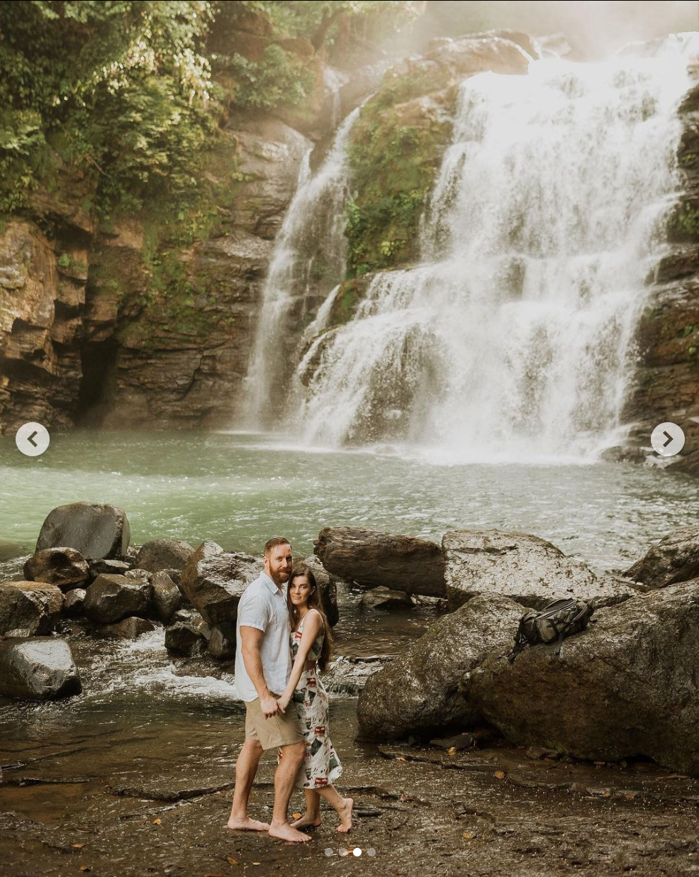 Couple standing together on rocky terrain in front of cascading waterfall.