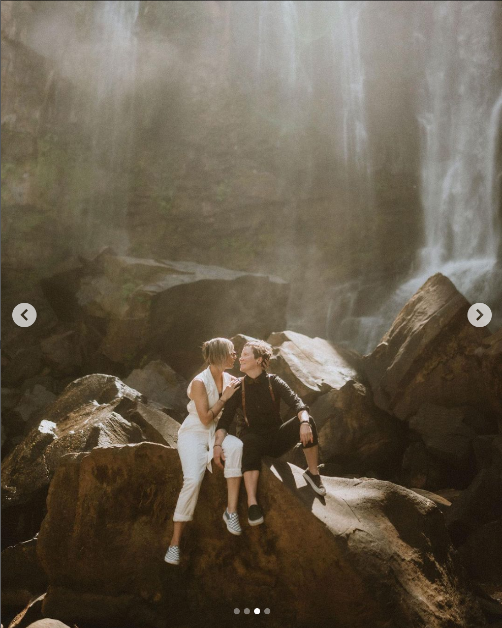 Intimate moment shared between couple on rocky cliff by misty waterfall.
