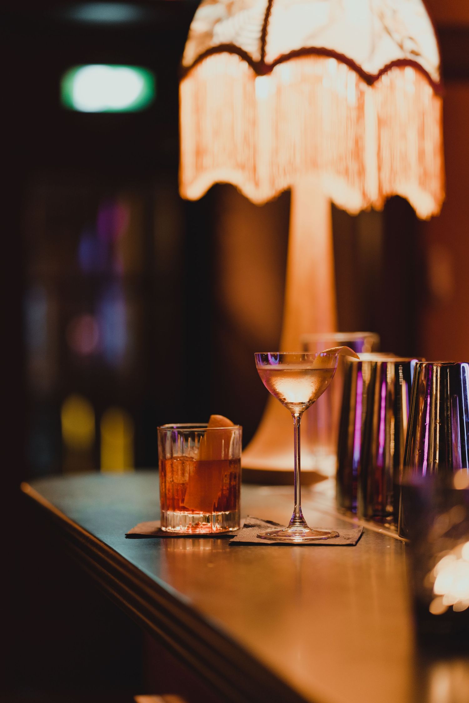 Cocktail glasses and vintage lamp creating moody ambiance at an upscale bar.