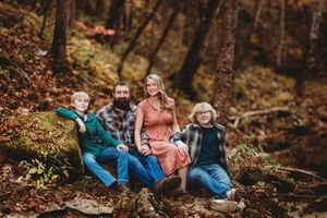 Professional portrait of mother, father, and two sons sitting on a rock in the woods of Alamosa, Colorado.