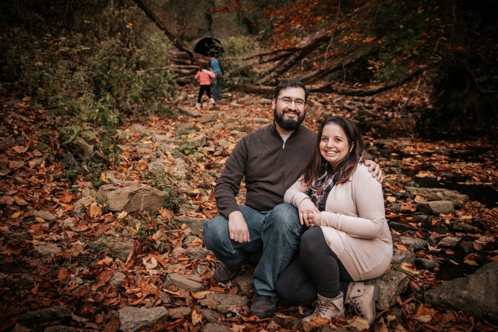 Husband and wife pose for the camera while their children are exploring woods in background.  Gunnison, Colorado.