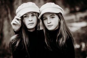 Two sisters in white hats with arms around each other while having their professional portrait taken.