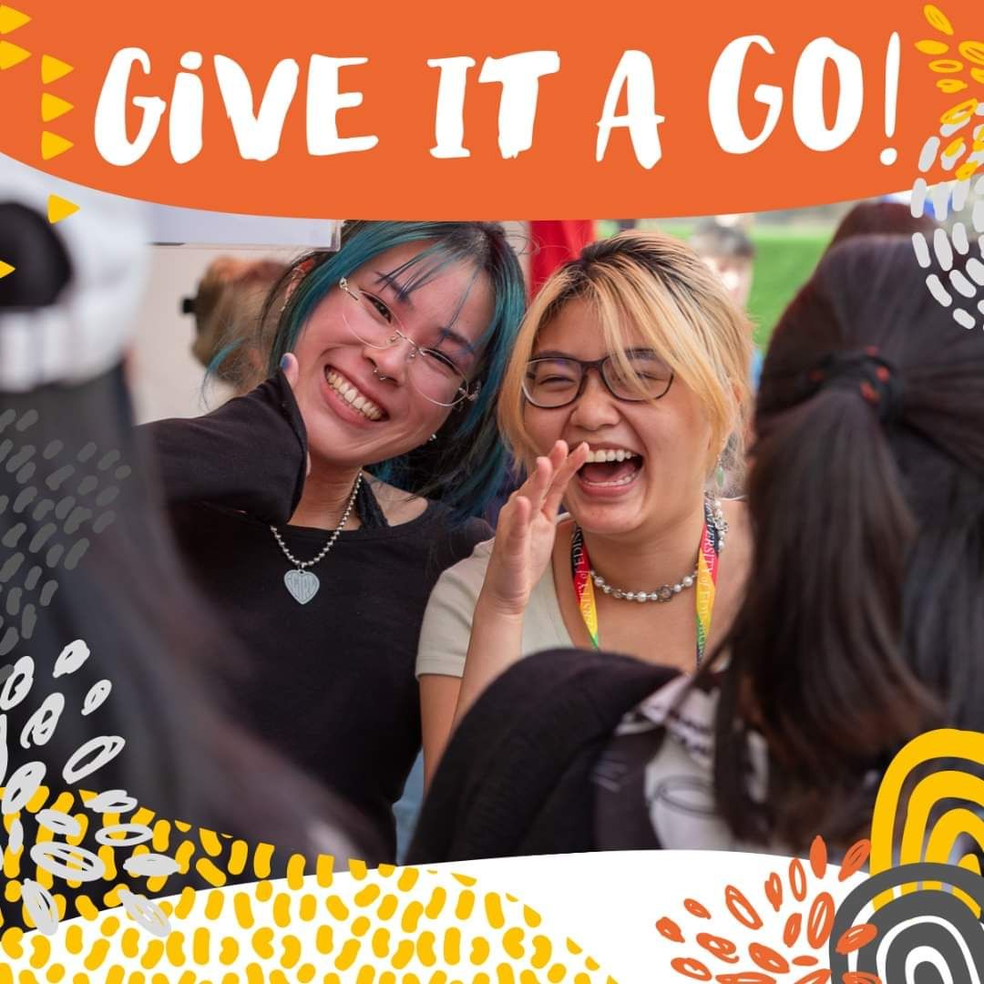 Two friends sharing a laugh at an outdoor event with orange banner decorations.