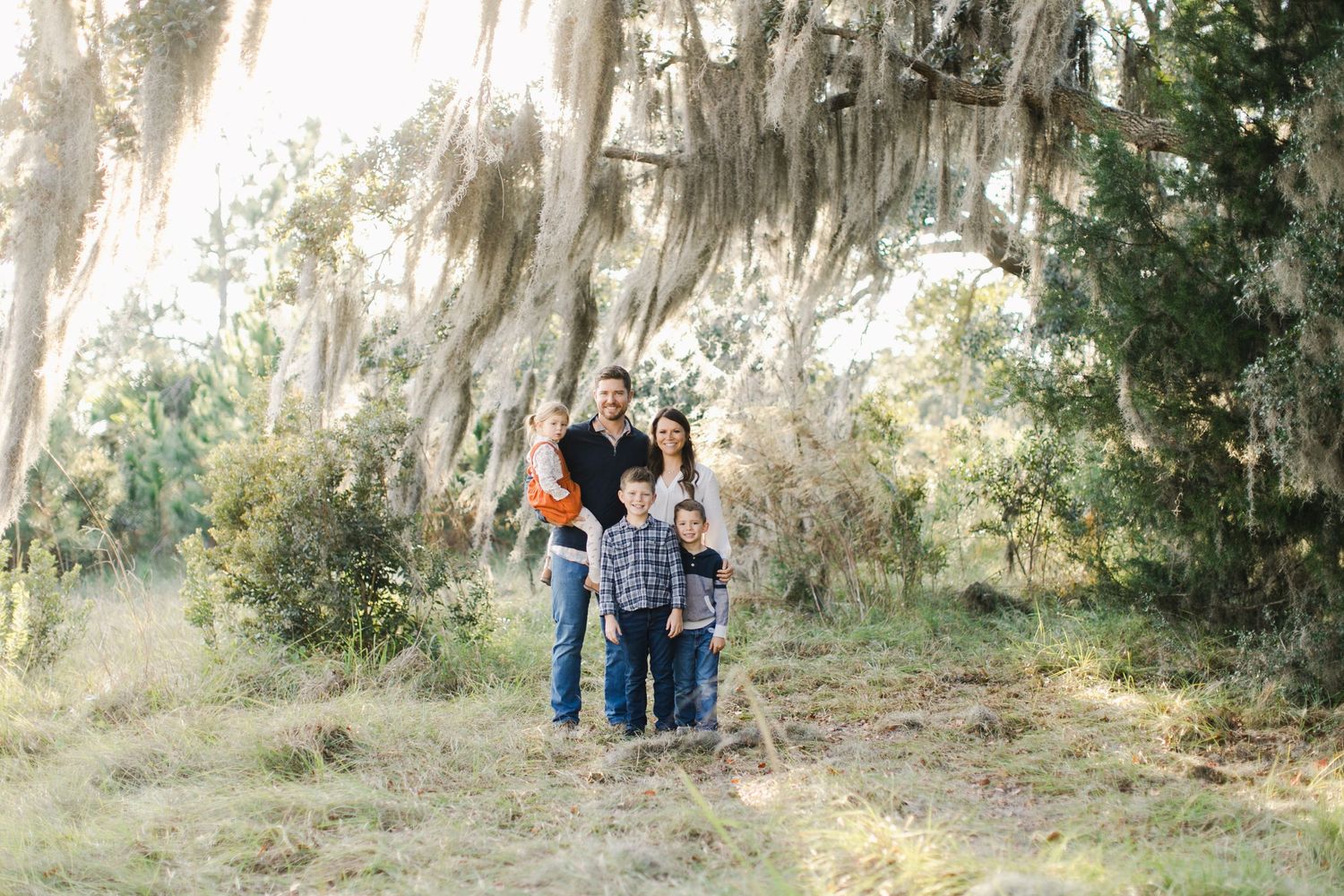 Family walking together under majestic oak trees draped with Spanish moss in Beaufort, South Carolina while posing for photography session.