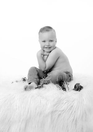 Black and white portrait of a smiling baby sitting on fluffy white fur.