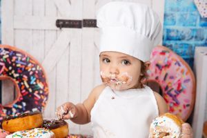 Young chef in white hat and apron surrounded by colorful donuts.