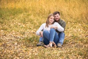 Couple sitting together on fallen autumn leaves in a golden field.