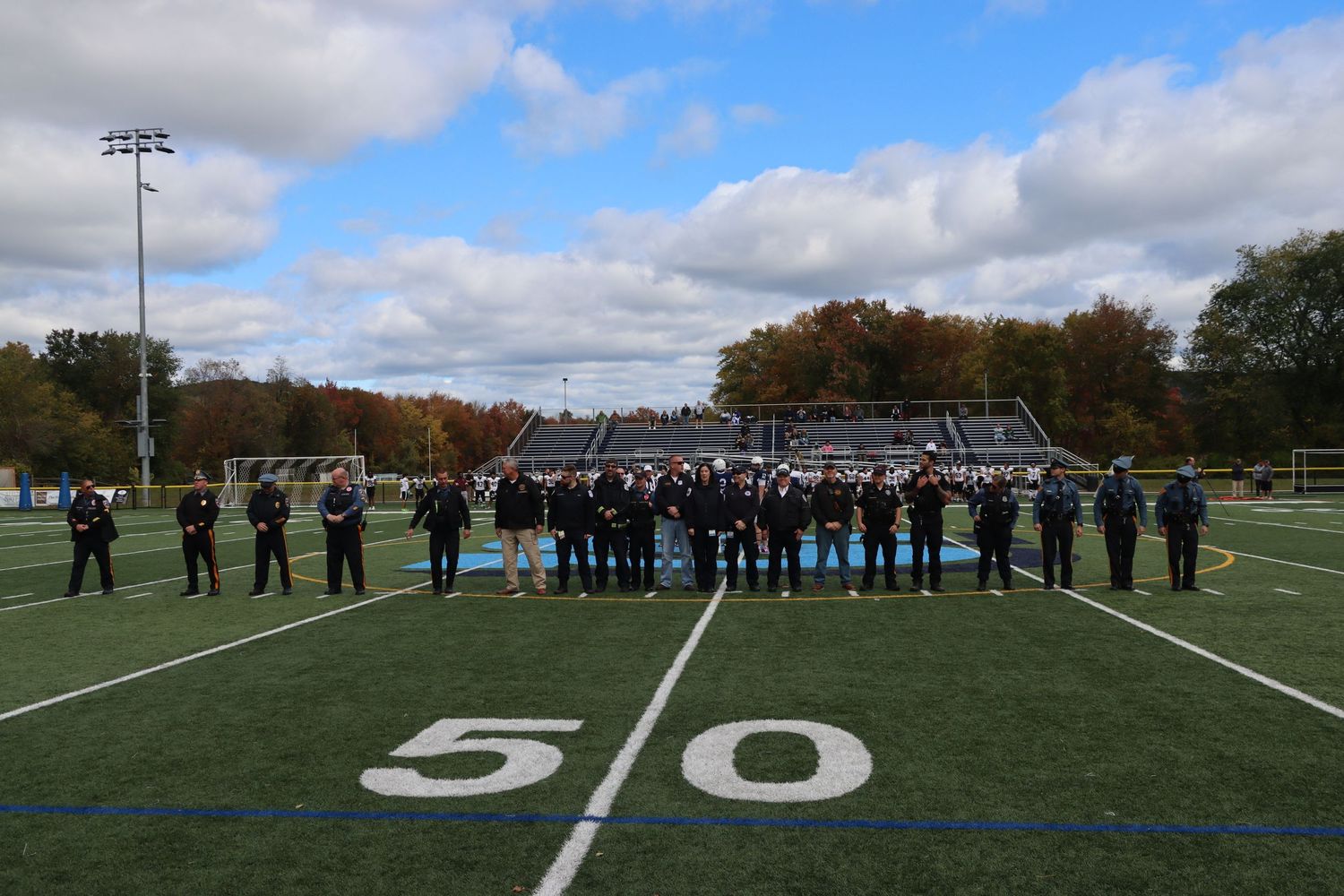 A marching band lined up on the 50-yard line of a football field in autumn.