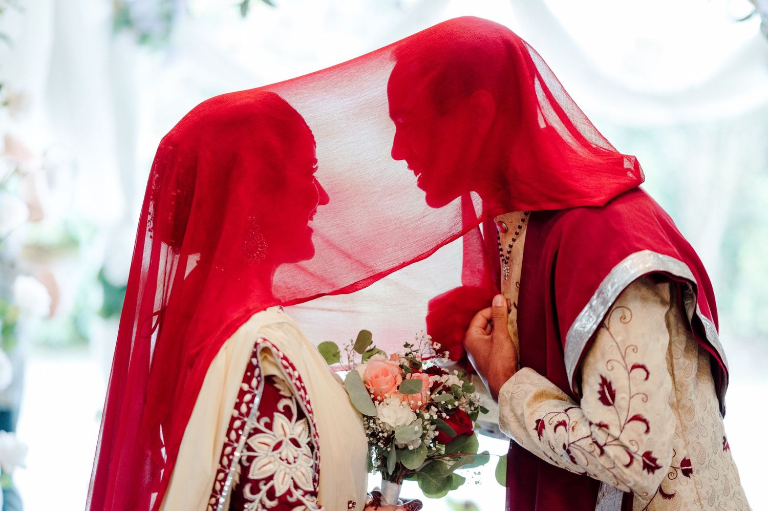 Bride and Groom smile under red veil.