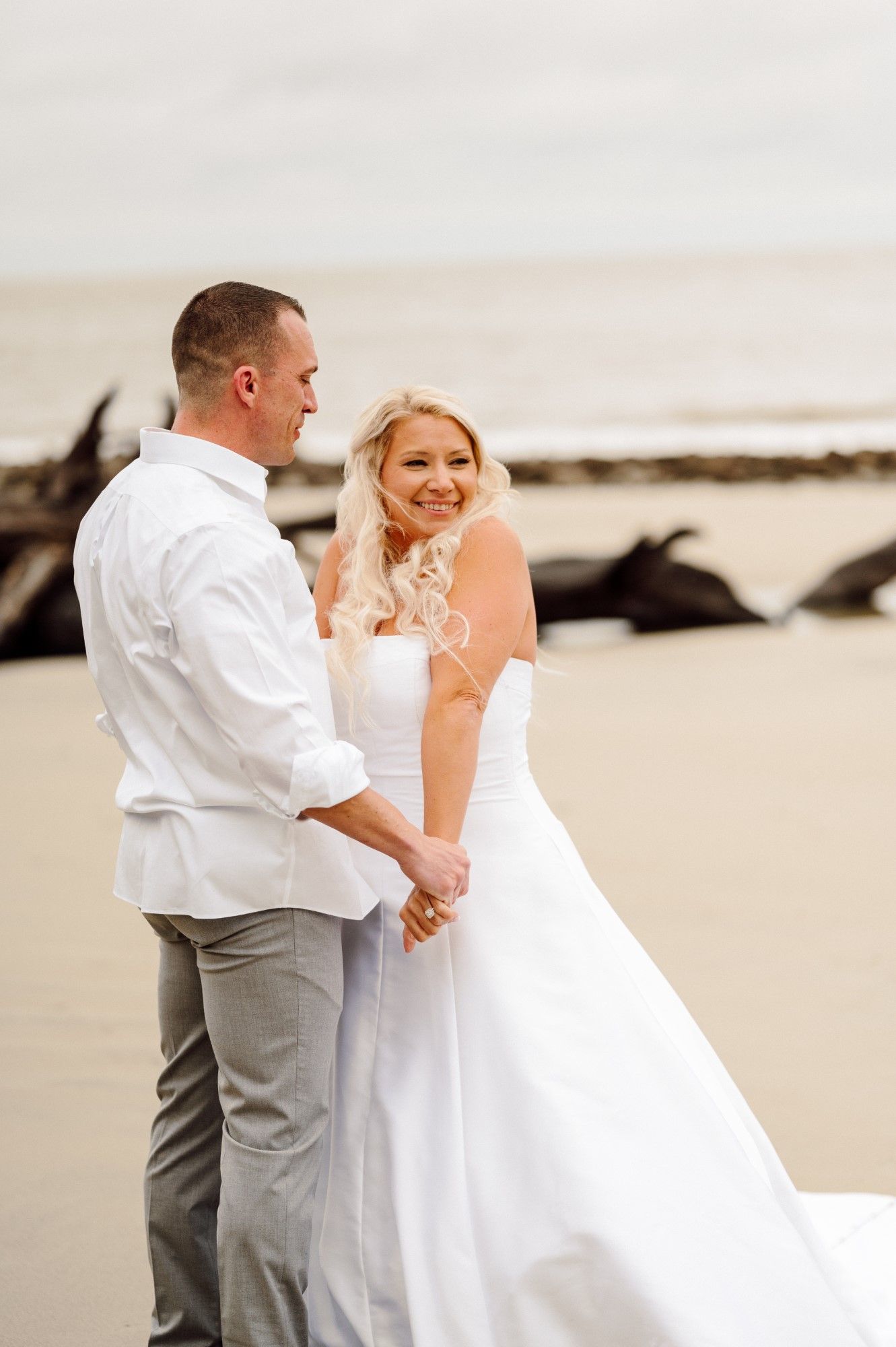 Bride and Groom smile on driftwood beach.