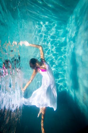 A woman in a white dress underwater poses like a ballerina