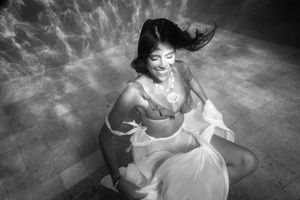 A woman smiling at the bottom of a pool in a white dress