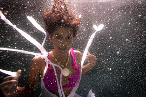 A woman falling through water with white dress straps floating