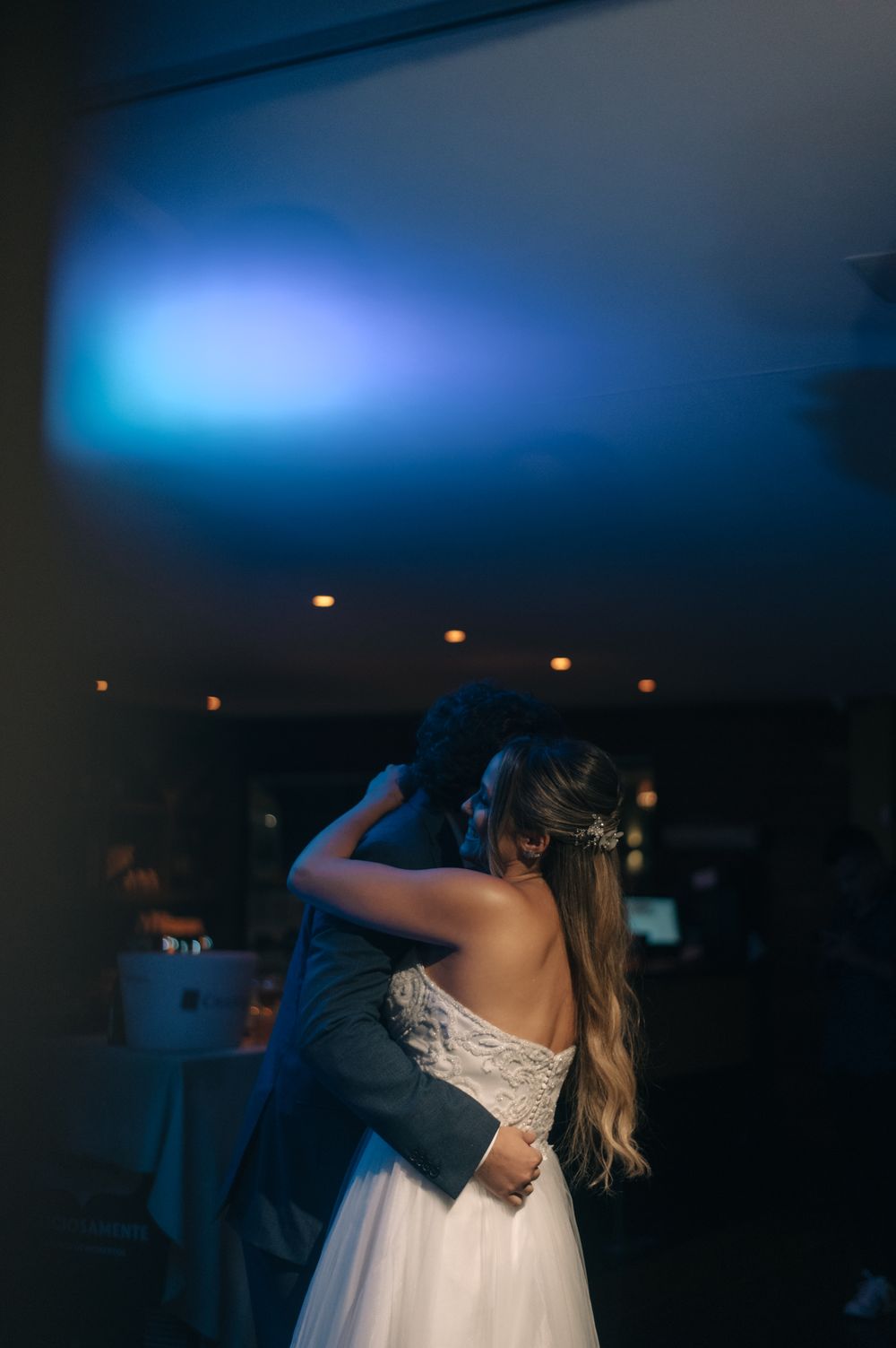 Couple dancing under blue mood lighting at wedding reception, bride in white dress and groom in dark suit.