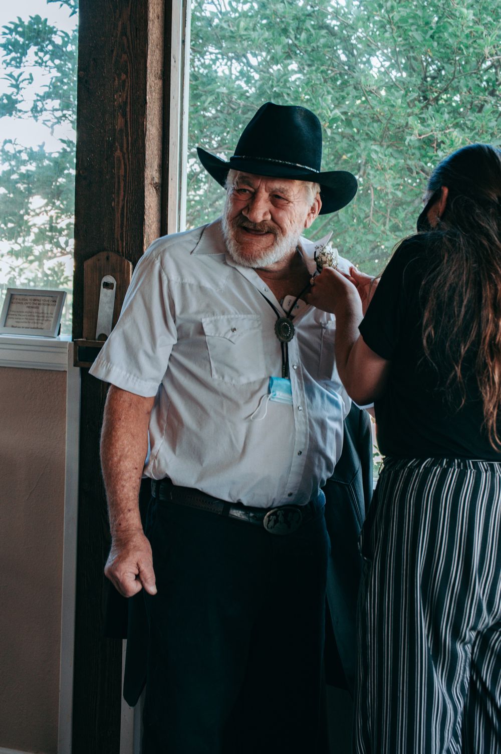 A smiling older man in a black cowboy hat and white shirt at a wedding celebration.