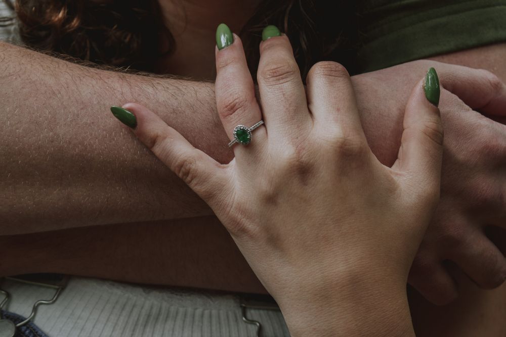 Close-up of a woman's hand with green nails and a green gemstone ring resting on a man's arm.