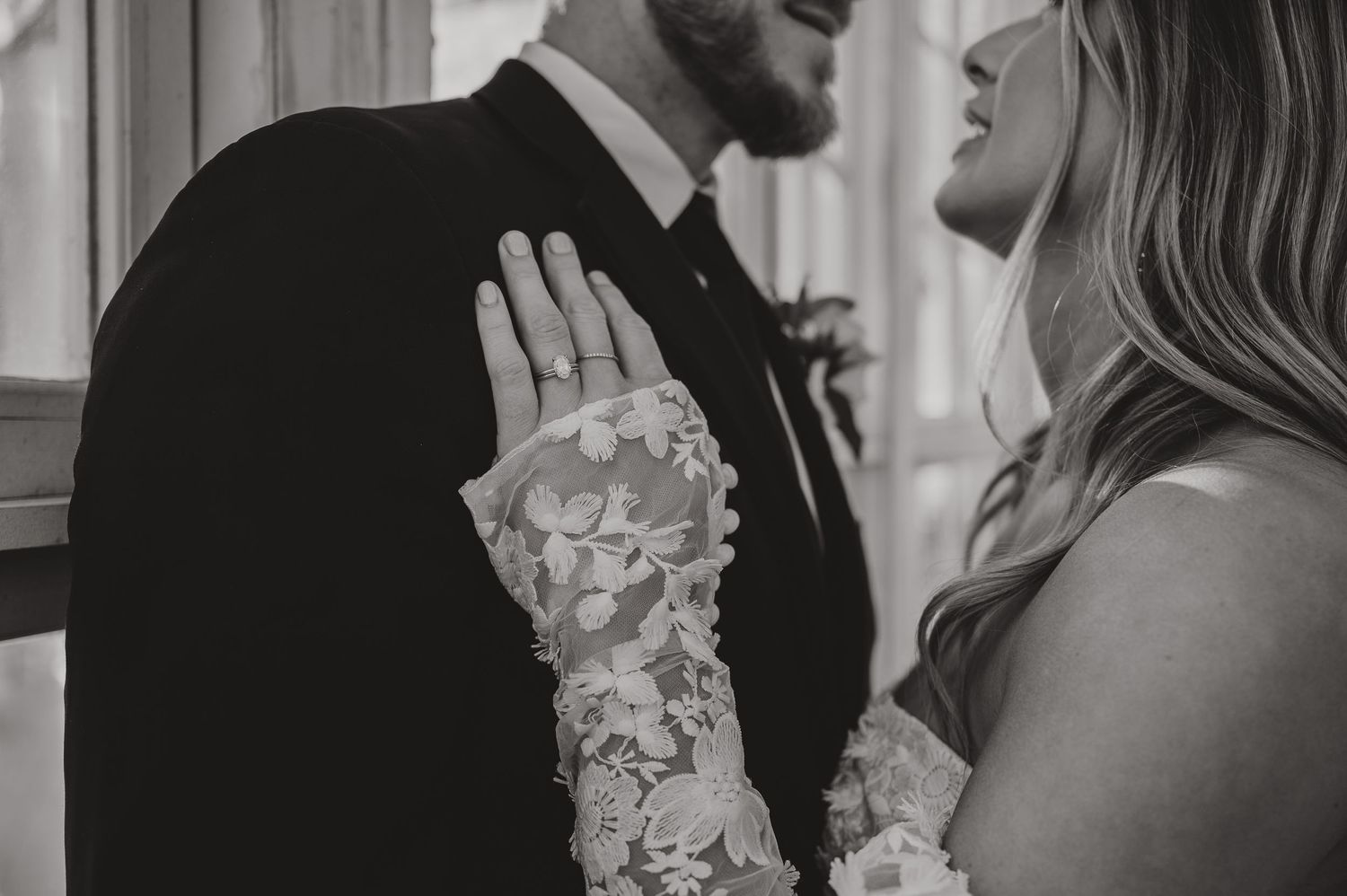 Black and white close-up of intricate lace sleeve details against groom's suit.