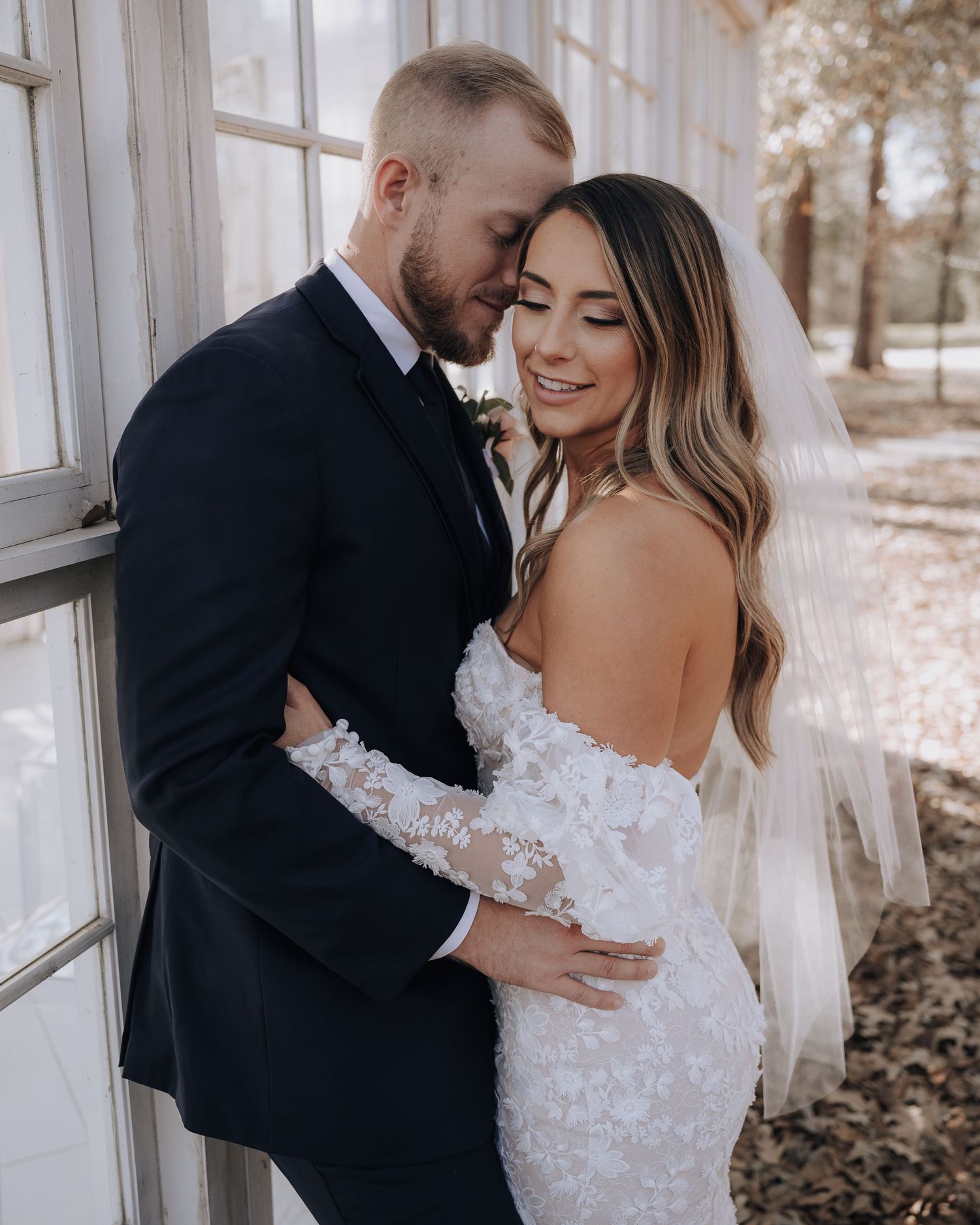 Romantic wedding portrait against white greenhouse windows with natural lighting.