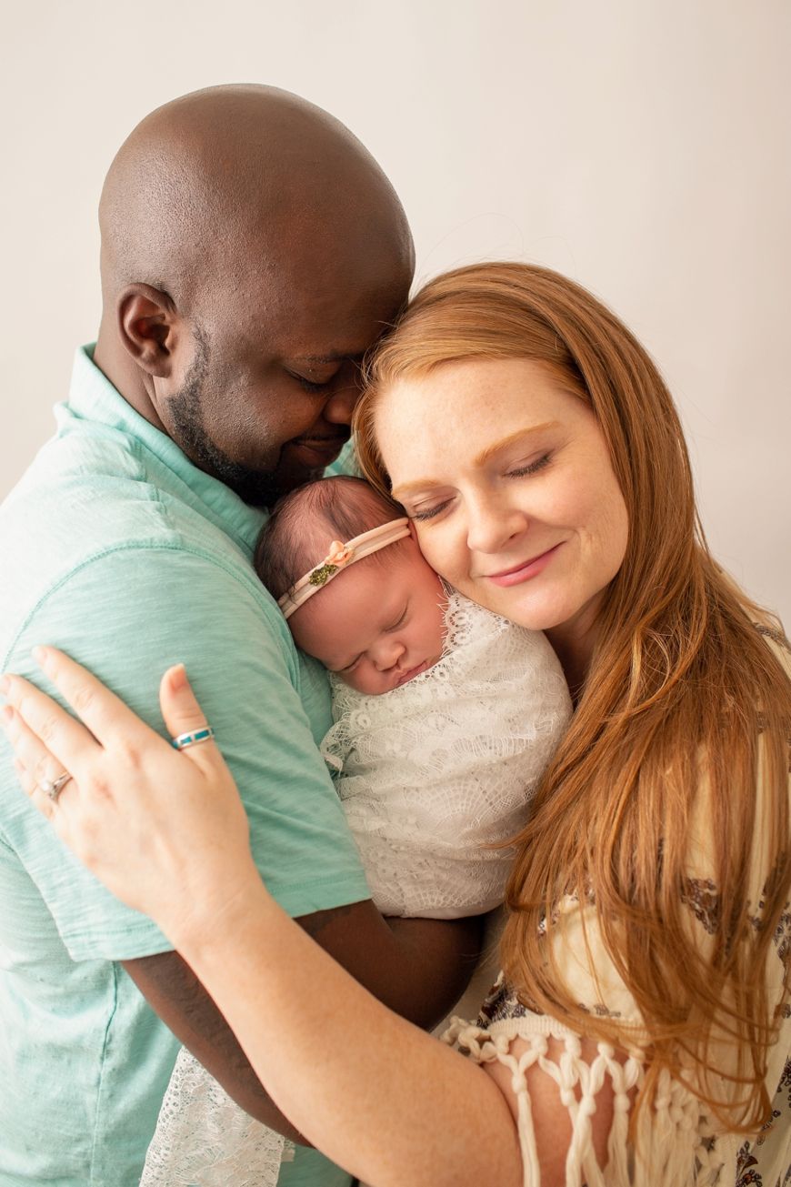Family shares an intimate moment embracing their newborn baby against light background.