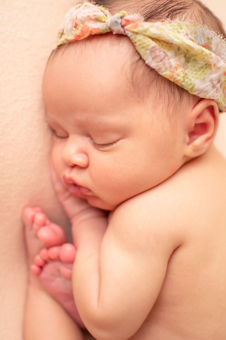 Close-up of sleeping newborn with floral headband against peachy backdrop.