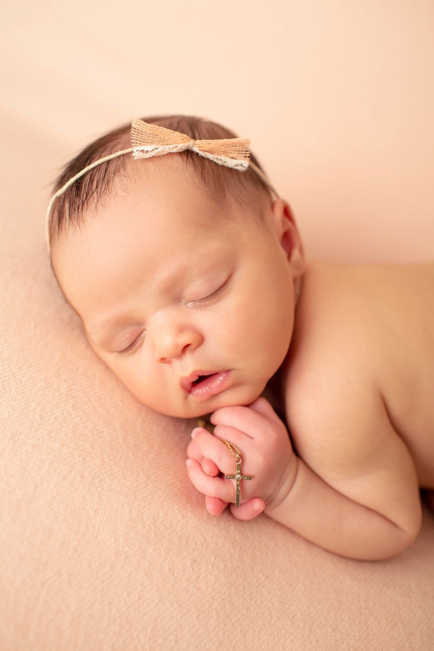 Peaceful sleeping newborn with bow headband resting hand near face.