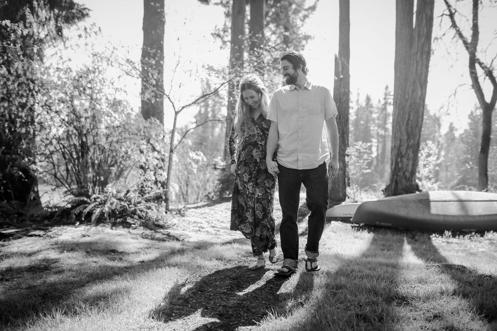 Black and white photo of a couple walking hand in hand through a sunlit forest path.