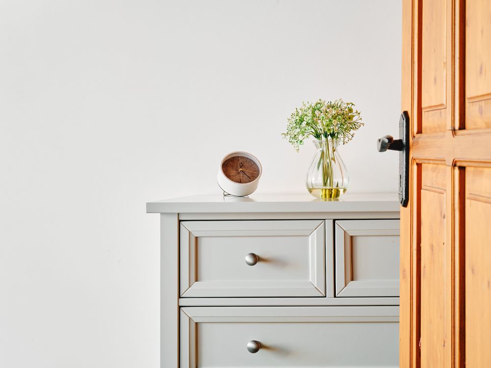 Minimalist grey dresser with small vase of flowers and wooden door frame.