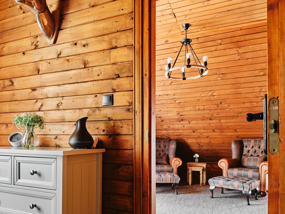 Rustic living room corner with wooden walls, white dresser, and modern chandelier.