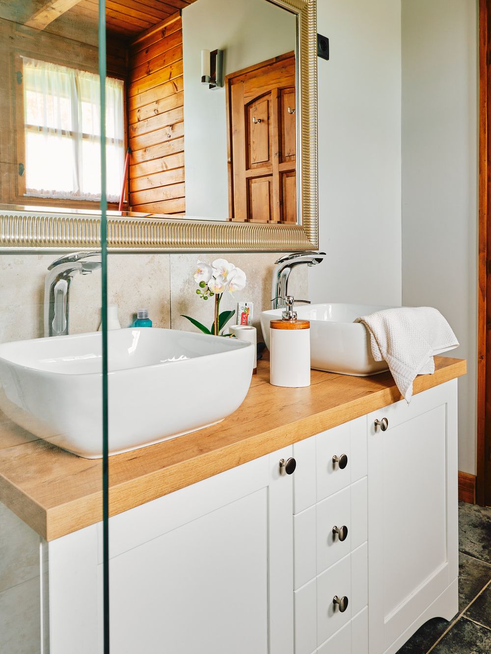 Contemporary bathroom vanity with white vessel sink on wooden countertop and glass mirror.