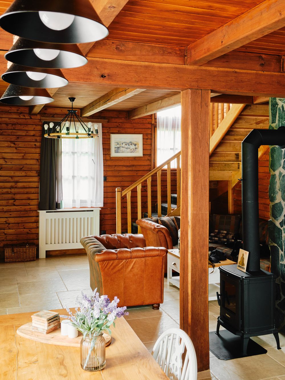 Cozy cabin living room with wooden walls, leather sofa, and black wood stove.