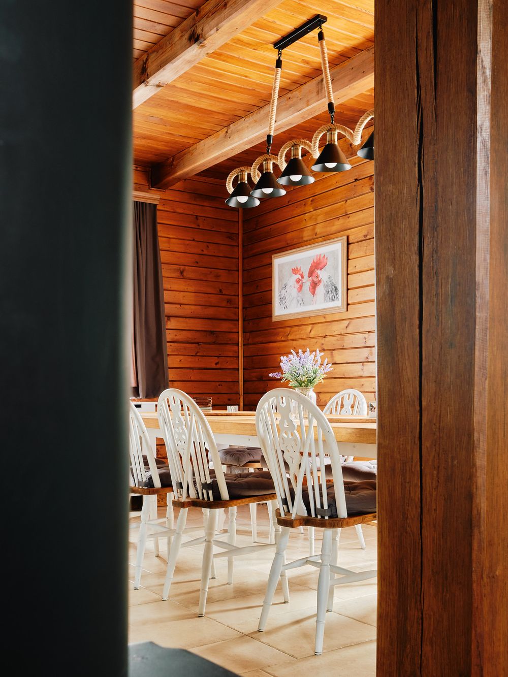 Rustic dining room with wooden walls, pendant lighting, and white chairs.