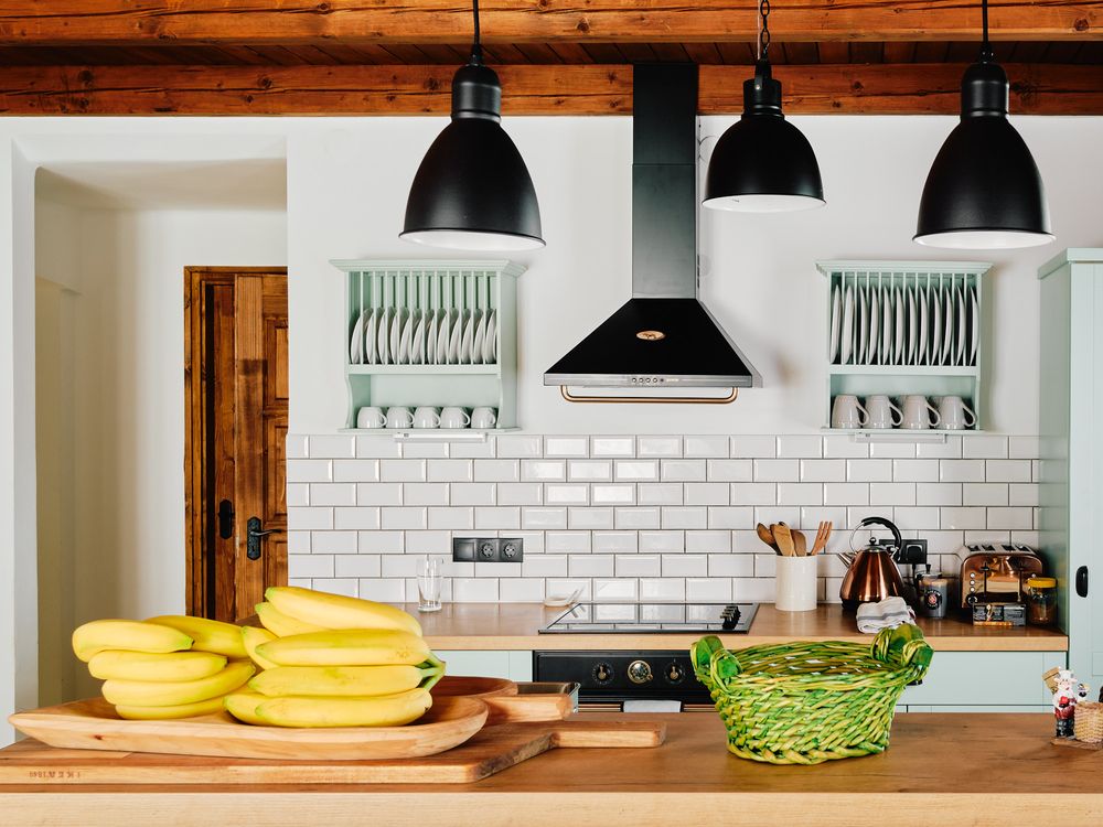 Modern kitchen with white subway tiles, mint cabinets, and bananas on wooden counter.