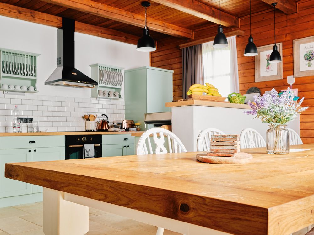 Bright kitchen featuring mint cabinets, wooden table, and black pendant lights.