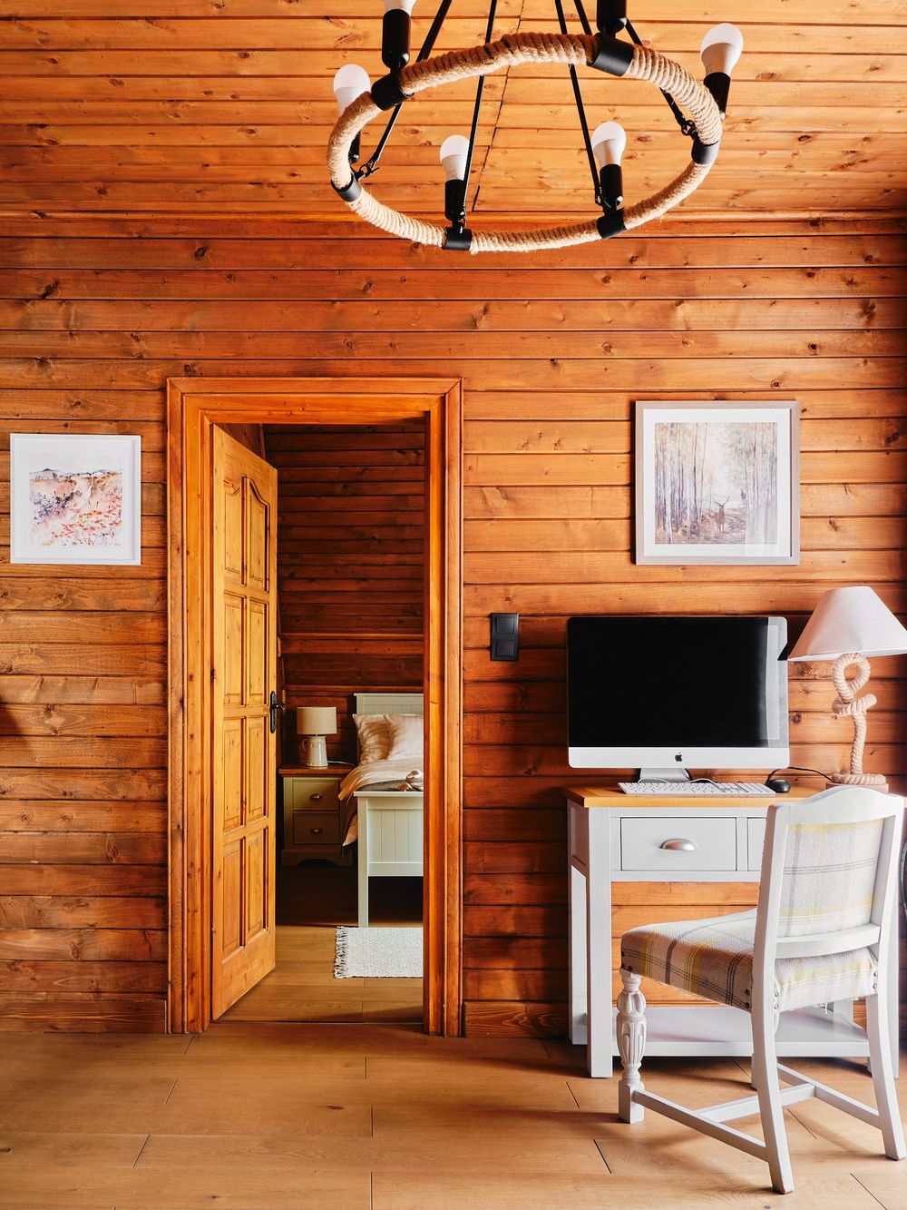 Cozy wooden room interior with chandelier, white desk setup and natural pine wood paneled walls.