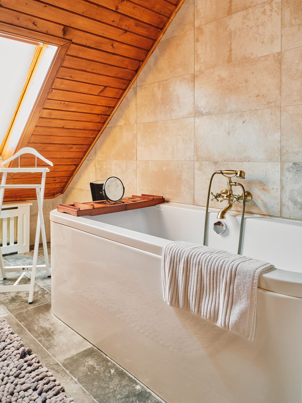 Attic bathroom with slanted wooden ceiling, freestanding tub, and brass fixtures.