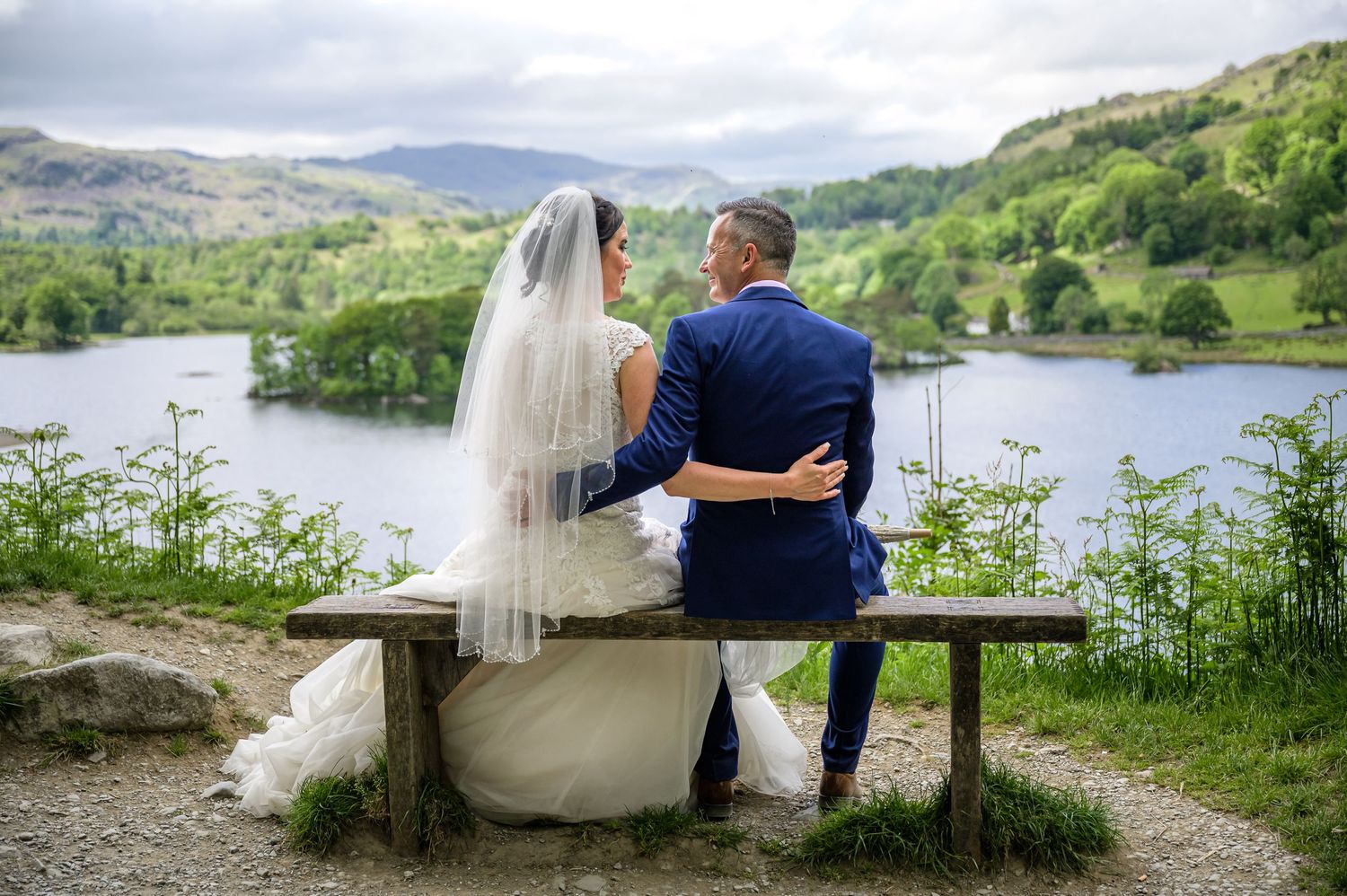 Bride and groom sitting on bench overlooking Rydal Water in Lake District