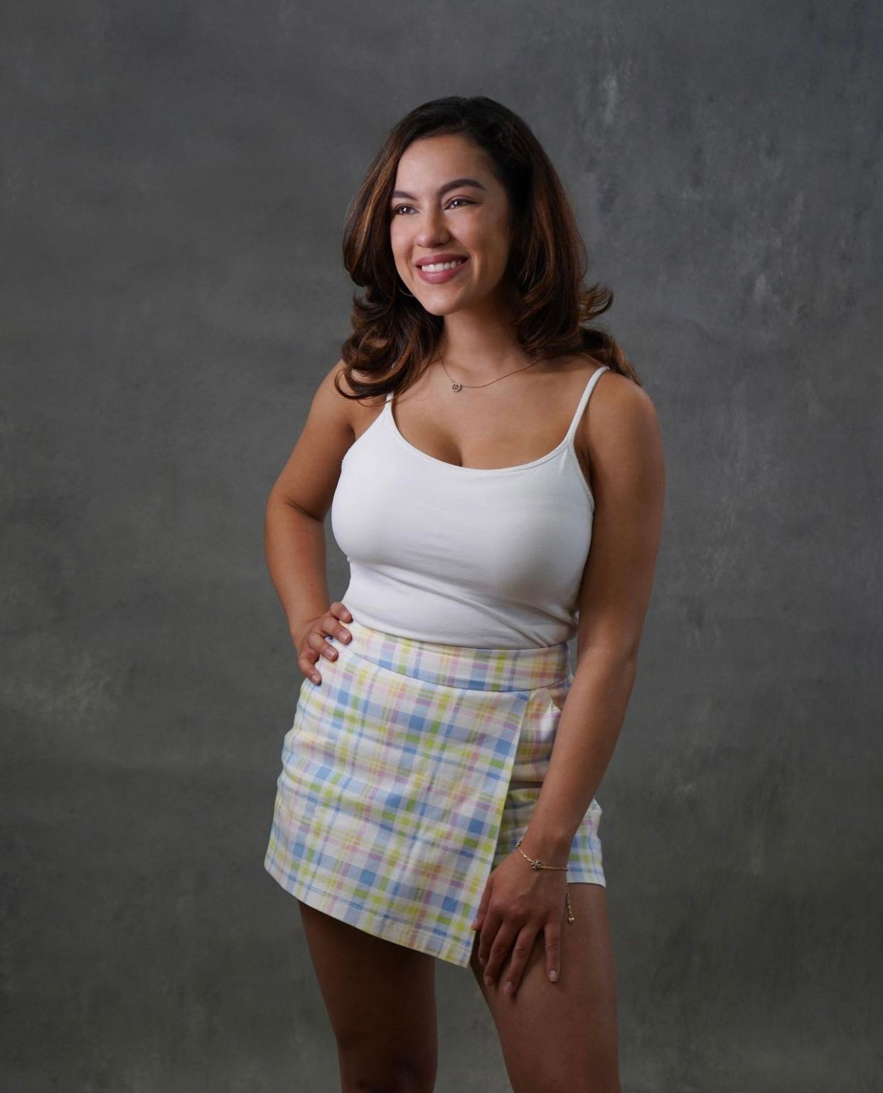 Client in white tank top and plaid fabric posing against dark background.