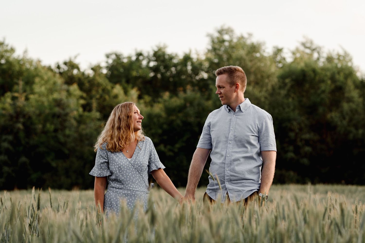 Couple walking hand in hand through a wheat field at dusk.