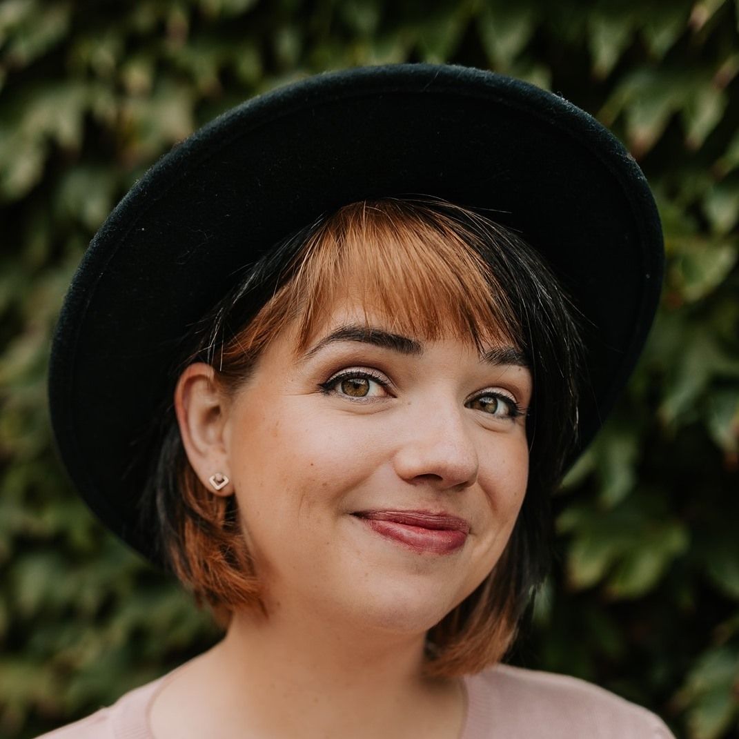 Portrait of person wearing black hat against green foliage background.