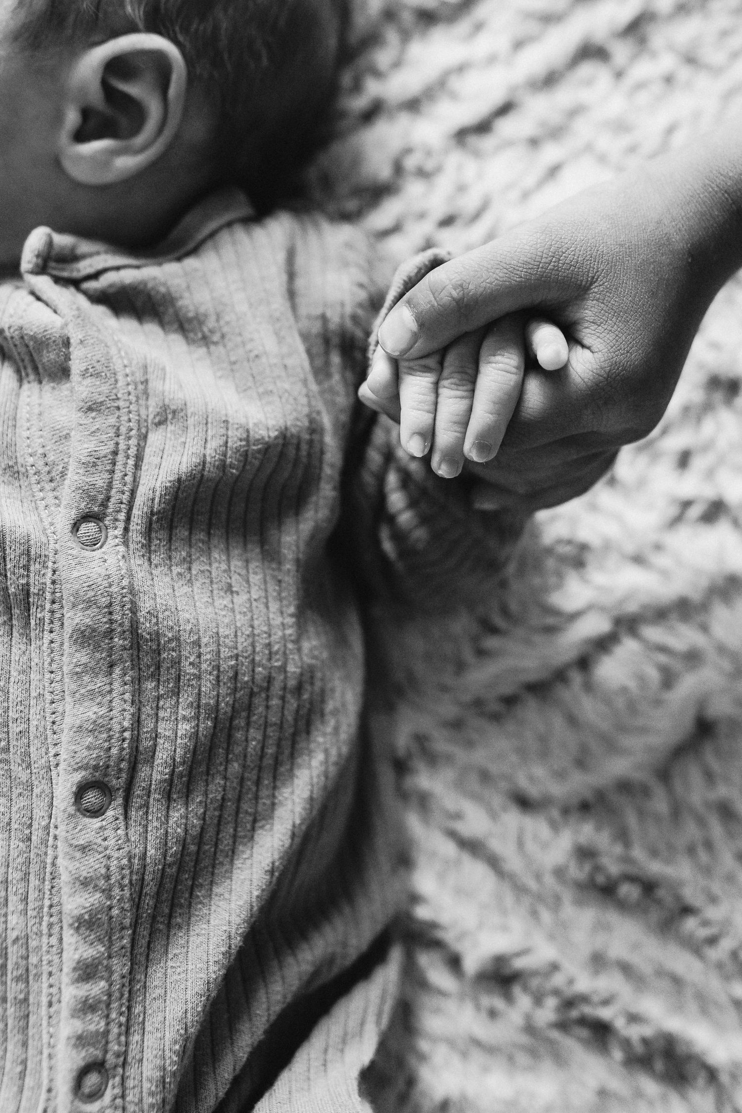 A black and white photos of a newborn babies hand holding his older sisters hand