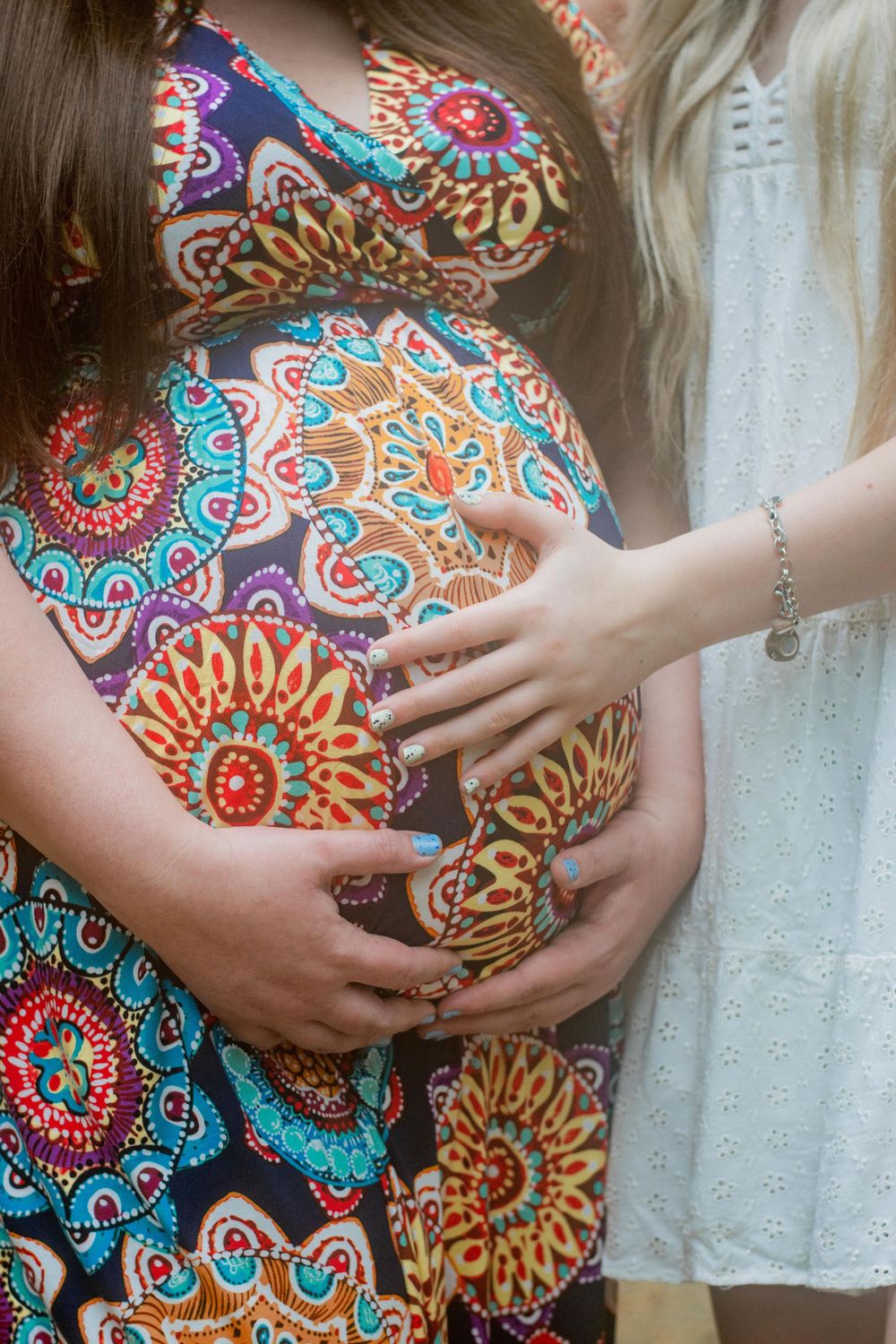 Close-up of hands cradling a pregnant belly in colorful floral print dress.