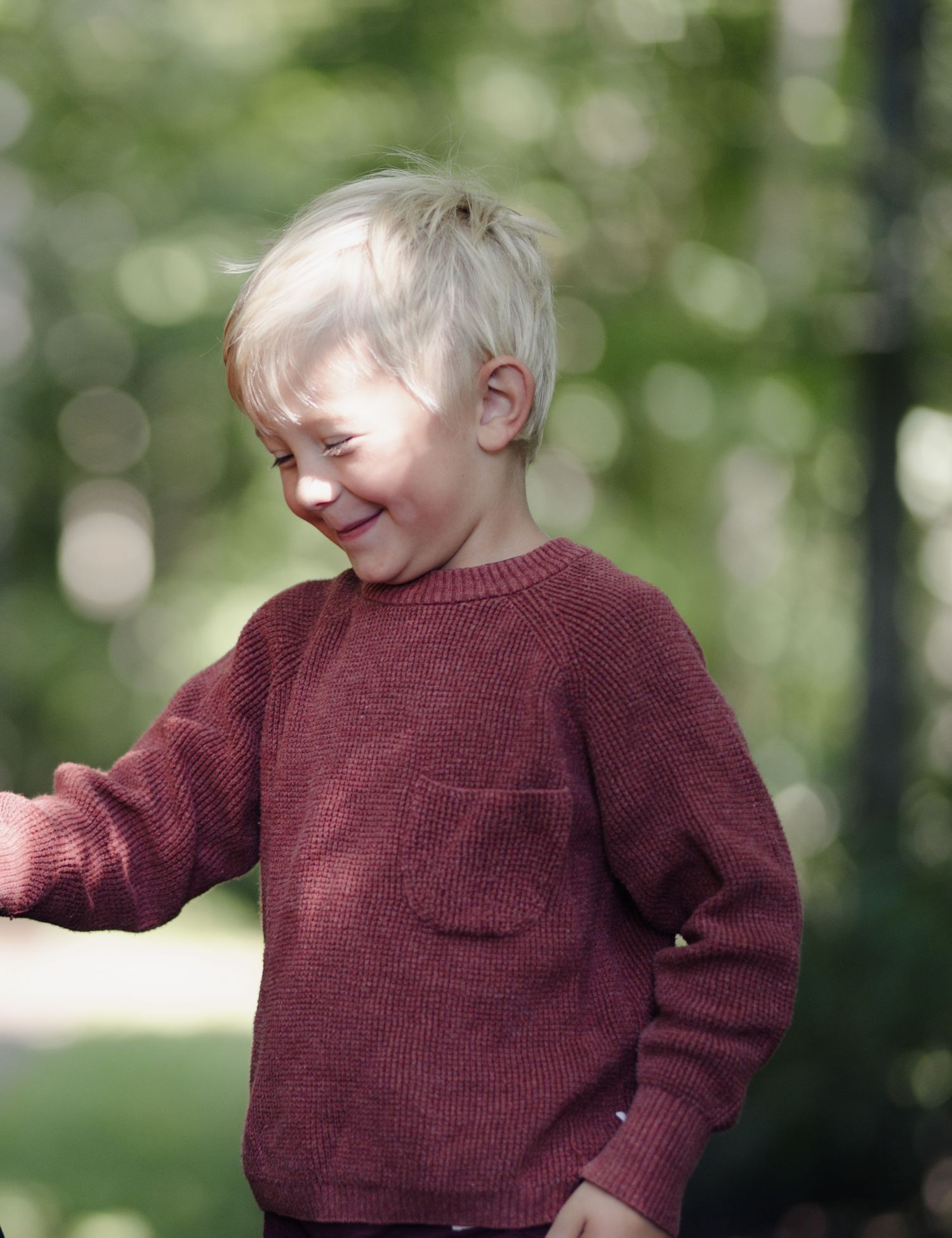 Candid shot of child laughing while wearing maroon sweater outdoors.