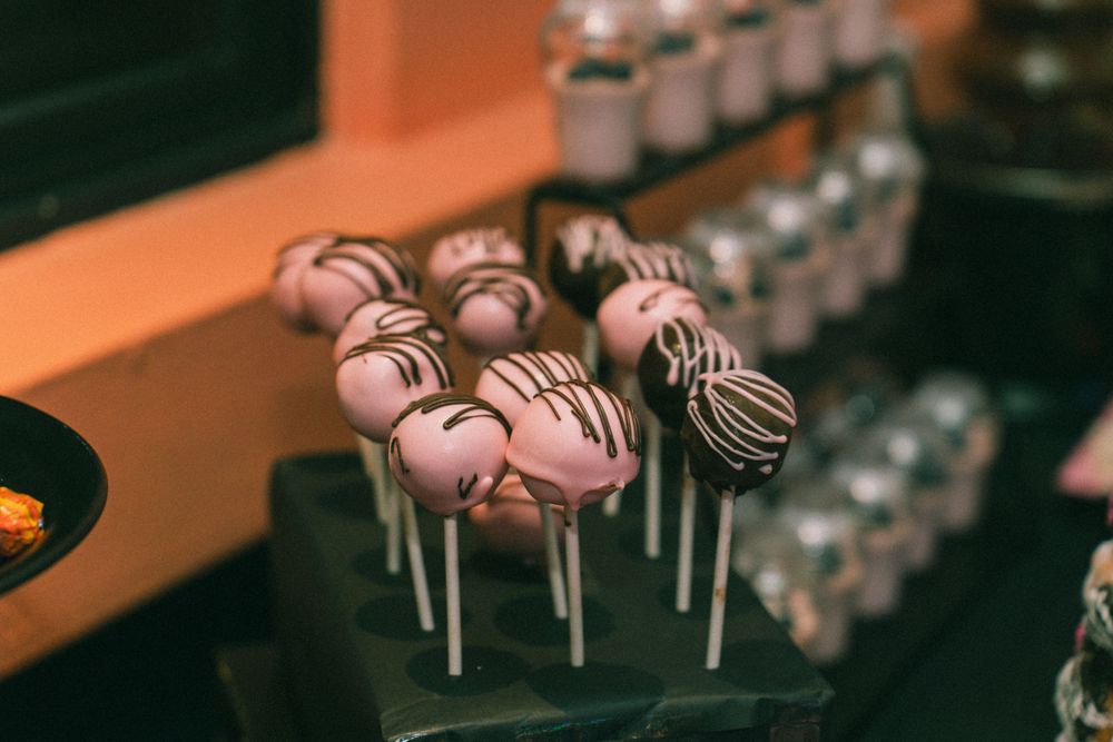Pink cake pops decorated with chocolate drizzle displayed on sticks.