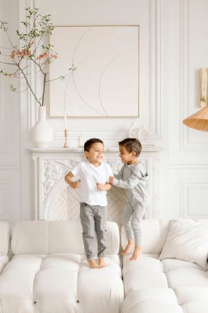 Two children playing and jumping on white couch in bright minimalist room.
