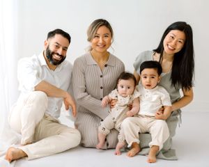 Family of five poses together in casual white outfits against neutral background.
