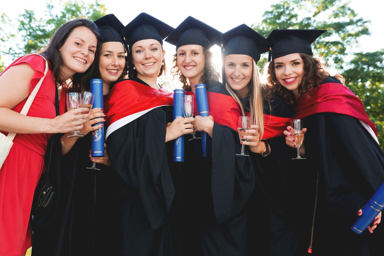 Group of graduates in caps and gowns celebrating with champagne outdoors.