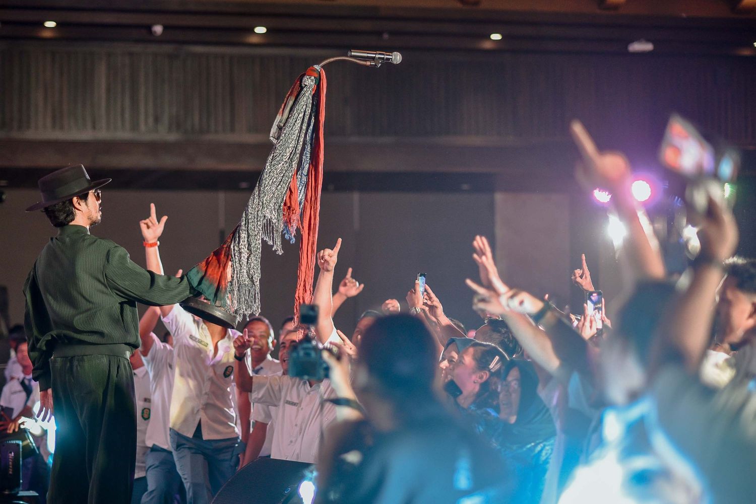 Concert crowd raises hands in excitement as performer interacts from stage.