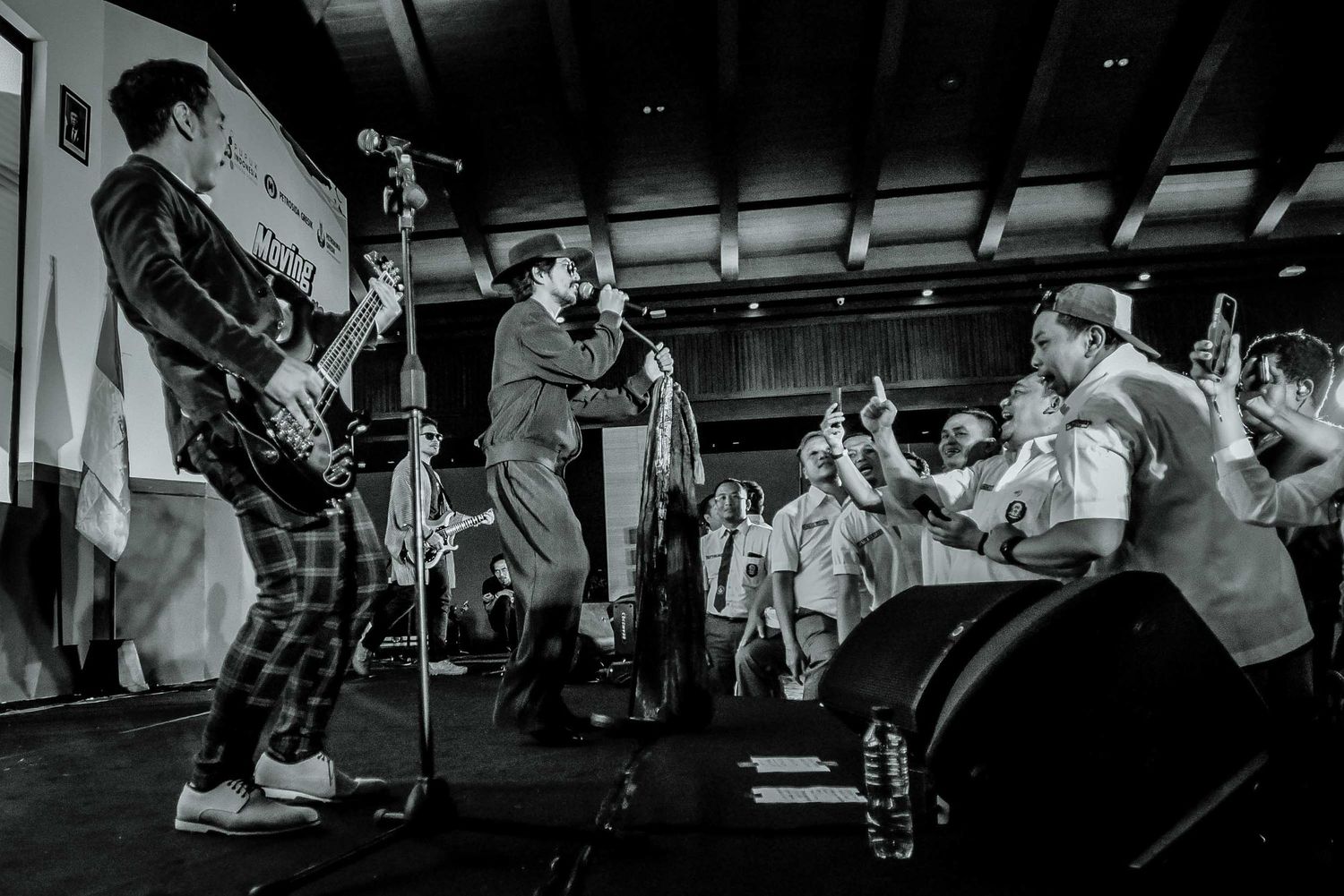 Black and white shot of energetic band performing on stage with crowd in foreground.
