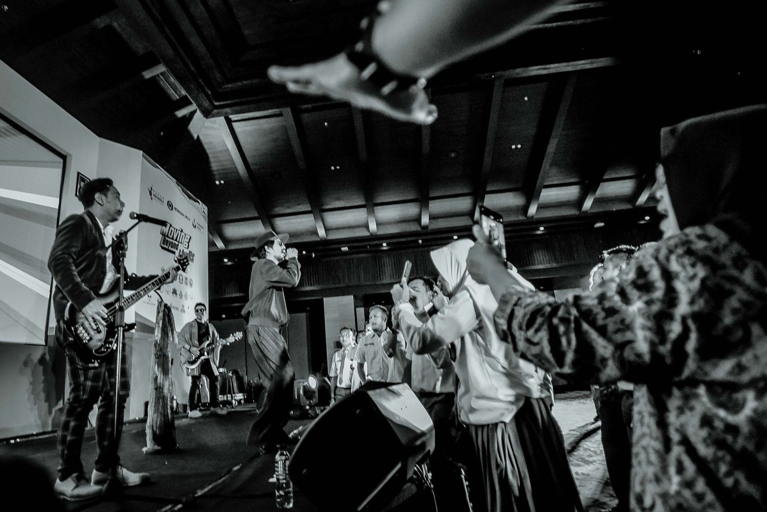 Energetic concert scene with performers and audience in black and white photography at an indoor venue.