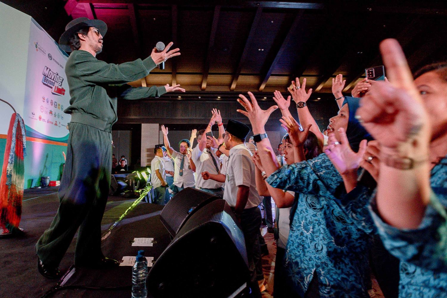 A performer on stage interacts with an enthusiastic crowd raising their hands during a live show.